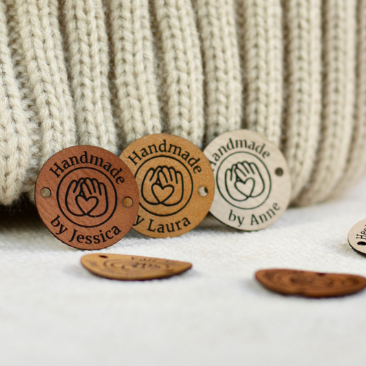 Handmade faux leather tags with engraved text and hand symbol on a knitted fabric background