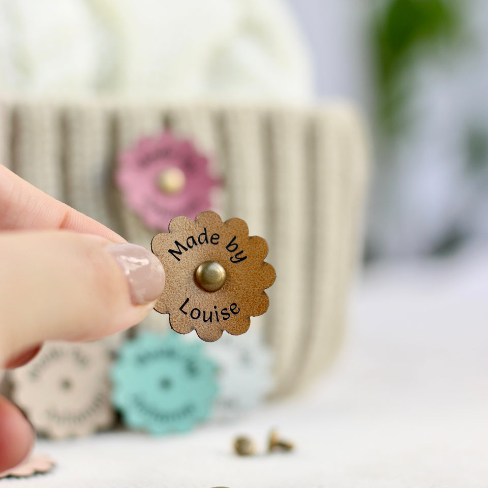Floral crochet tags with a 'Made by Louise' text held by a hand against a blurred background.
