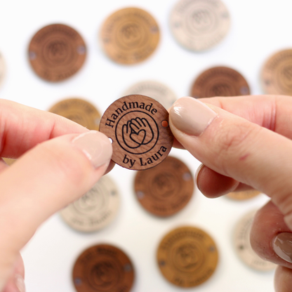 Faux Leather Tag with 'Handmade by Laura' text held between fingers against a blurred background of similar badges.
