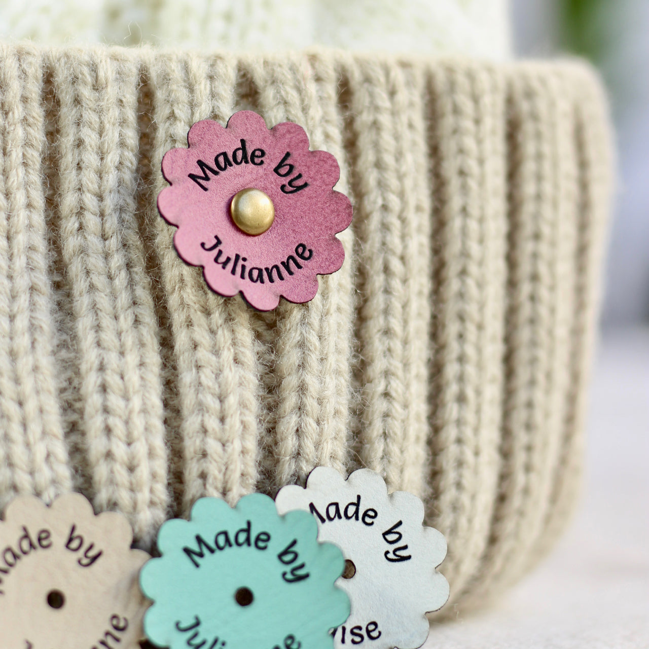 Flower-shaped 'Made by Julianne' tag on a knitted item with other similar tags.