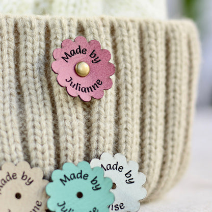 Flower-shaped 'Made by Julianne' tag on a knitted item with other similar tags.